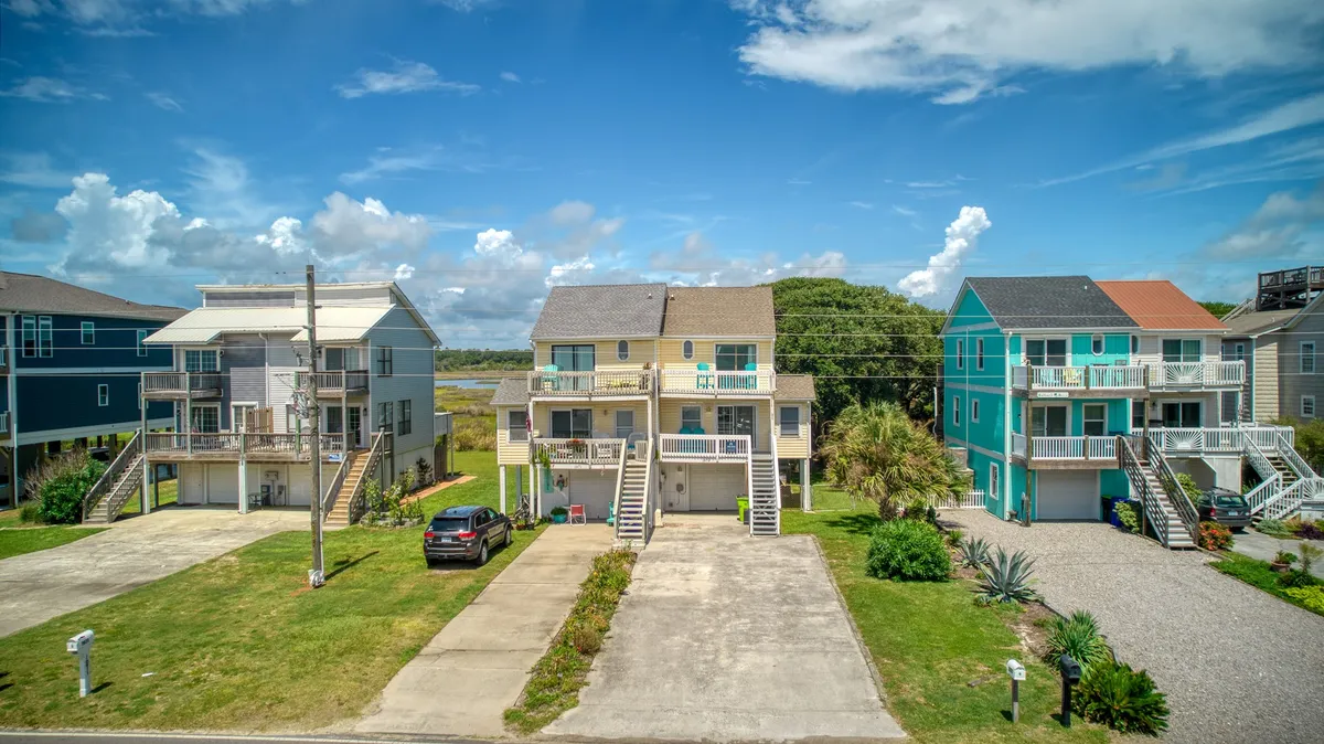 A cheerful exterior shot of colorful houses framed by palm trees, with a driveway and blue sky overhead. The inviting scene hints at a lively beach neighborhood, ideal for families gathering or setting out for local adventure.