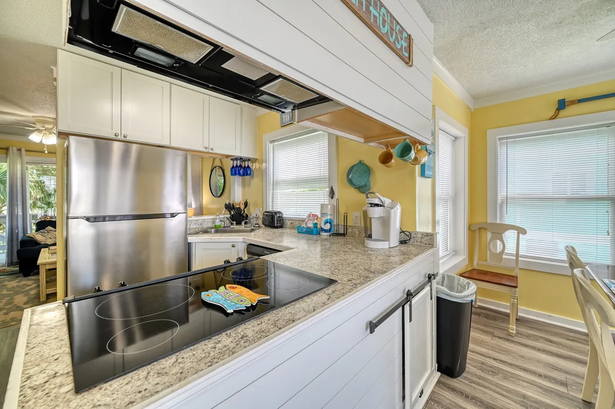 A modern kitchen with stainless steel appliances, granite countertops, colorful dishware, and a lighthearted kitchen sign. The space is well-lit and primed for preparing family meals or hosting friends.