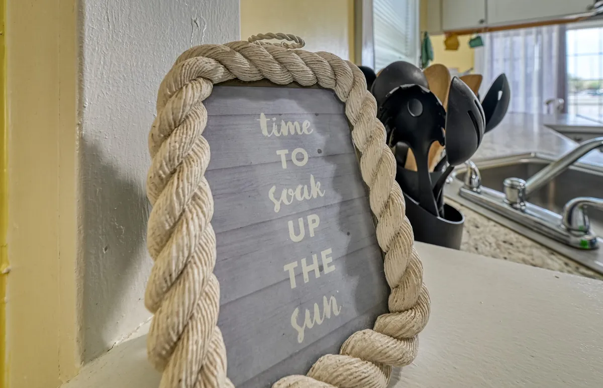A cheerful kitchen countertop scene with a framed sign, utensils, and casual decor, evoking a welcoming environment for cooking, socializing, and relaxation. The setup suggests a homey space where guests can enjoy casual brunches or laid-back afternoons.