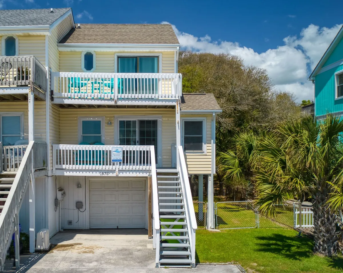 An exterior view showcasing balconies with turquoise furniture, palm trees, and a glimpse of the yard below. The presence of green space and seating evokes a sense of outdoor living and play.