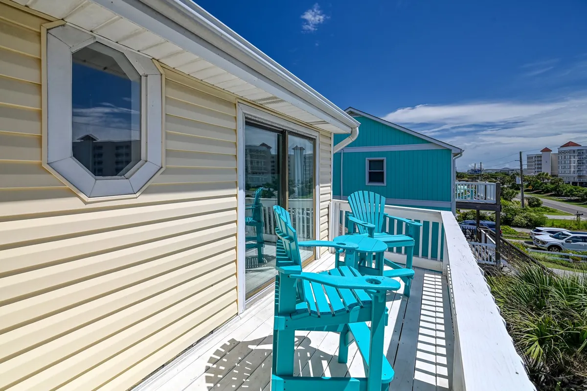 A front deck with turquoise chairs, a glass sliding door, and an octagonal window. The outdoor seating is positioned for enjoying the breeze, socializing, or watching the sunset, encapsulating the transition between interior and exterior living spaces.