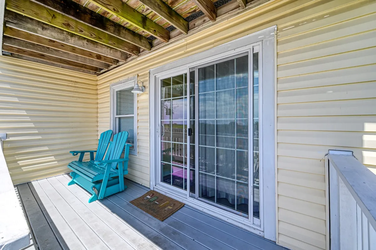 This image captures an inviting outdoor porch space featuring turquoise rocking chairs, a sliding glass door leading inside, and a wooden ceiling above. The tranquil atmosphere is enhanced by views of the outdoors and a setting perfect for relaxing in the sun or enjoying a cool evening breeze.