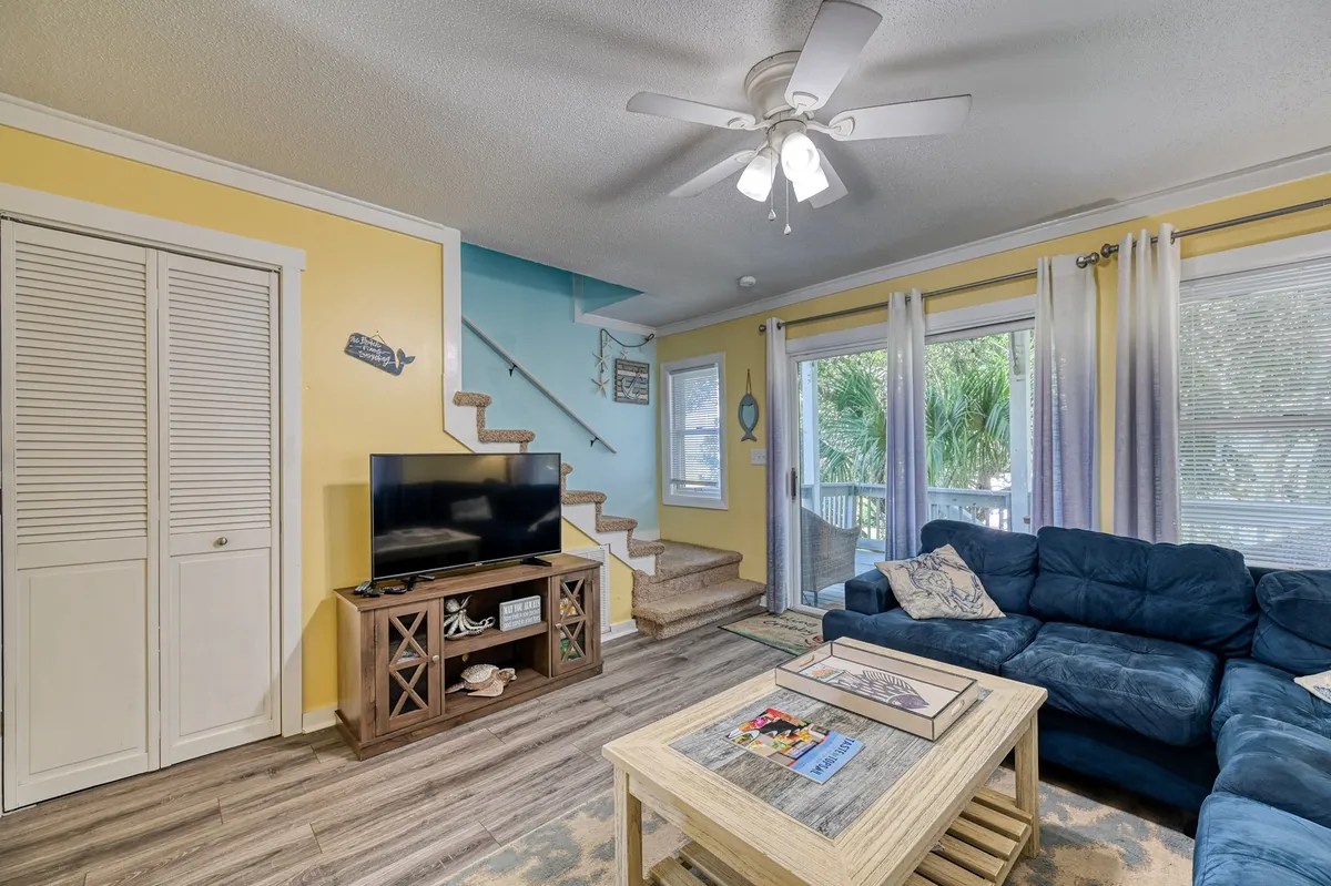 A casual living area with a blue couch, wooden coffee table, television, and sliding glass doors to let in natural light. The arrangement suggests a comfortable space for relaxing, watching TV, or gathering with friends and family.